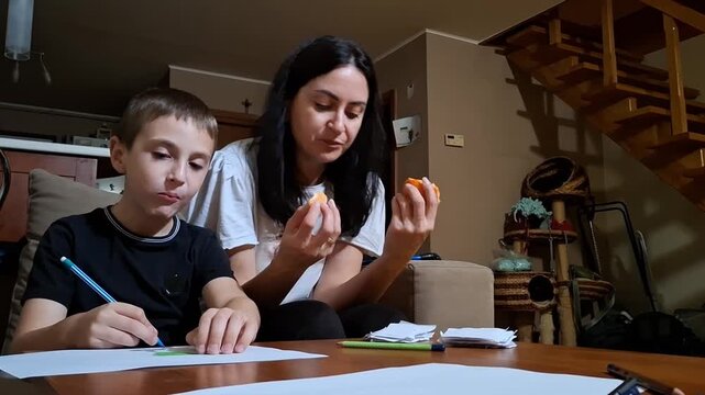 7 year old boy draws while sitting with an adult and eating snacks at home in the evening
