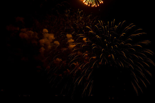 Bright, golden fireworks illuminate the dark night sky, creating an enchanting scene above a city. Explosive bursts of light form patterns contrasting with the surrounding darkness, highlighting a fes