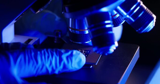 Slow motion close up microscope inspecting AI microchip on laboratory stage with gloved hand, modern factory.