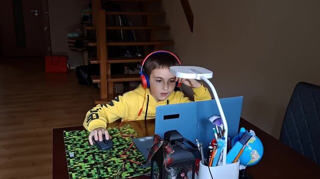 Boy playing on computer with headphones at home