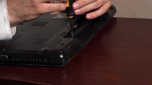 Technician disassembling a black laptop case with a precision screwdriver for repair and maintenance.