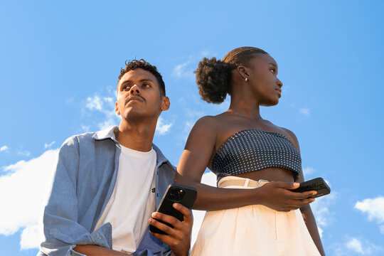 Young People Standing Outdoors With Phones in Bright Sky. Copy space