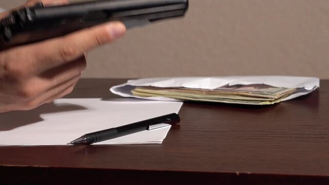 Unloading and handling a black pistol over a table where money and a white sheet of paper are lying.