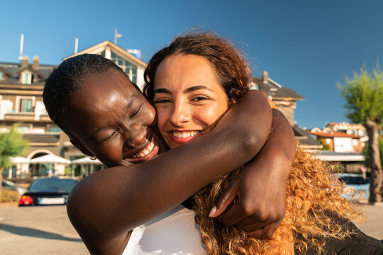 Two Female Friends Share a Hug in a Sunny Outdoor Setting