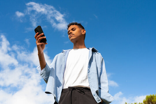 Young Man Checks Phone Under a Clear Blue Sky With Clouds. Copy Space