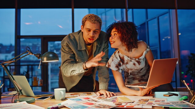 Multiethnic creative team analyzing color palette laptop late night studio.