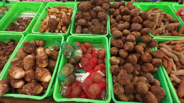 Assorted root vegetables and tubers, including taro, sweet potatoes, and yams, arranged in green plastic crates, showcasing fresh produce at a local market or grocery store