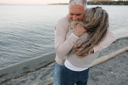 Older couple hugging on beach at sunset, candid emotional moment