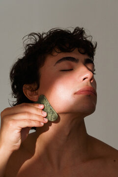 Man Uses Jade Roller on His Face in Indoor Setting