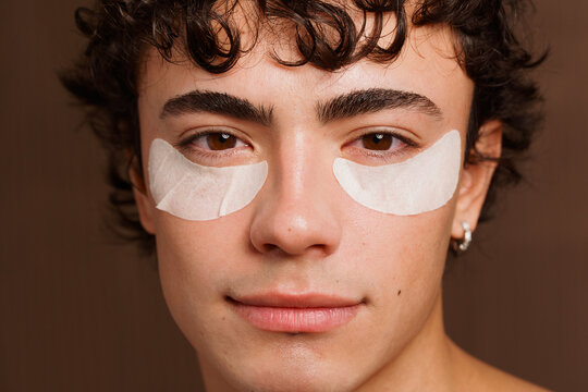 Young Man Applying Under-Eye Patches in a Studio Setting