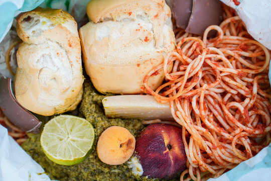 Discarded spaghetti, bread, fruit and leftovers fill a trash bag, illustrating household food waste, overconsumption and avoidable waste. 