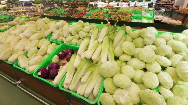 Supermarket produce section displays an abundant selection of fresh, organic vegetables, featuring green and red cabbages, endives, and other leafy greens, arranged in baskets for retail shopping