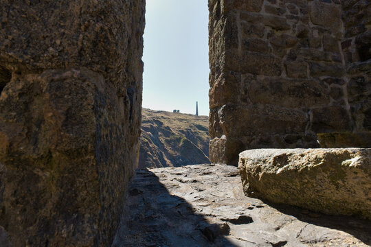 A sunlit view through old stone ruins, revealing a coast and a distant tower on a hill  - Botallack Mine & Engine House, Cornwall, UK