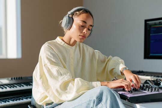 Young woman producing music in home studio with headphones and midi controller for music production background and creative workspace design