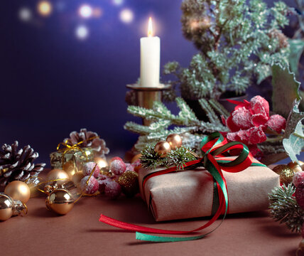 Christmas scene with handmade gift box with bow, candle, decorative fir branches, balls and cones for tree decoraton. New Year winter holiday composition with present, ornaments and decor.