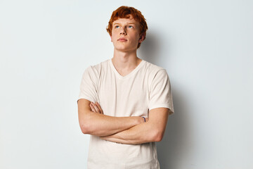 Young man with red hair wearing beige t shirt standing with arms crossed against light background...