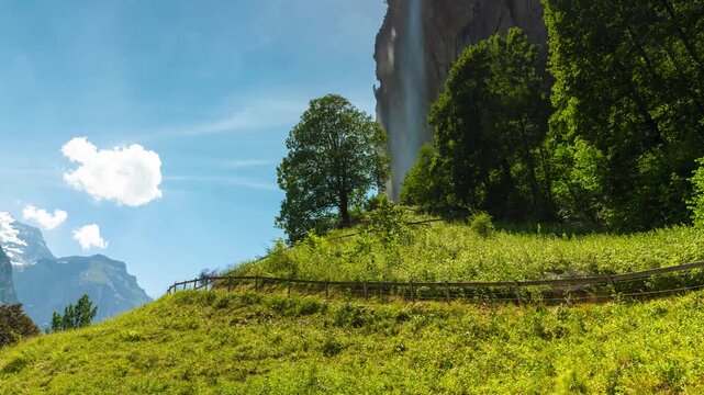 Rushing clouds over Staubbach waterfall in Lauterbrunnen Switzerland alpine valley during sunny day with flowing mist in mountain time lapse