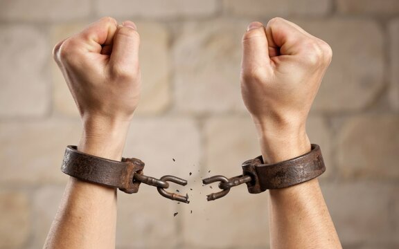 Human hands with broken iron shackles raised against a stone wall