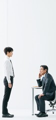 Obraz premium Employee standing talking with manager at desk. Young businessman standing next to blank space, talking with manager seated at white desk