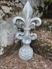 Decorative stone fleur de lis sculpture placed against old weathered stone wall © Оксана Жемеренко