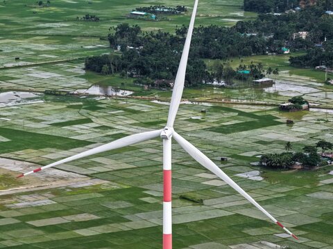 Aerial view of the Cox's Bazar 60 MW Wind Power Plant featuring a large wind turbine set against a backdrop of lush green rice paddies in Cox's Bazar, Chittagong Division, Bangladesh.
