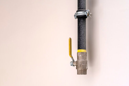 Insulated gas pipe mounted on a wall. Yellow ball valve and pipe clamp. Useful for plumbing guides, home improvement articles, and construction or building services content.
