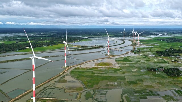 Aerial view of Cox's Bazar 60 MW US-DK Wind Power Plant with red and white turbines in flooded fields and green landscape in Cox's Bazar, Chittagong Division, Bangladesh.