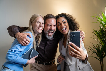 Obraz premium Diverse businesspeople smiling and taking a selfie together in a modern office, showing on social media teamwork and camaraderie between work. 