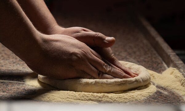 Close-up view of a chef's hands kneading fresh bread dough on a flour-dusted worktop. 