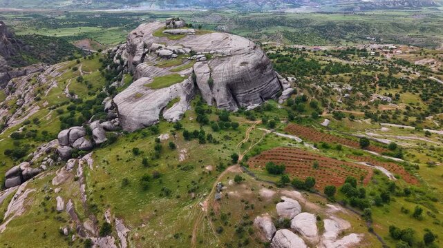 Smooth aerial flight turns left while passing close to a massive rock formation, revealing the vast green valley and dramatic rocky landscape beyond.