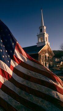 American flag waving before a historic wooden church at golden hour in a serene rural landscape