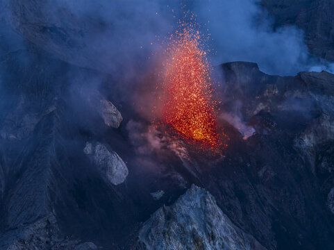 Aerial view of the active Stromboli volcano erupting with glowing lava fragments and volcanic ash plumes rising into the night sky over the Aeolian Islands, Lipari, Sicily, Italy.