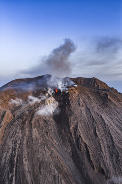 Aerial view of Stromboli volcano with volcanic smoke and glowing lava vents against a clear blue sky in Lipari, Sicily, Italy.