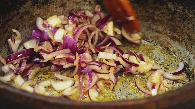 In a deep cast-iron skillet, chopped red onion is fried in vegetable oil
