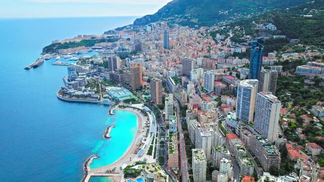 Drone view of Monaco&rsquo;s coastline. Dense city buildings, blue sea, harbour areas and mountain backdrop create a scenic Mediterranean panorama.