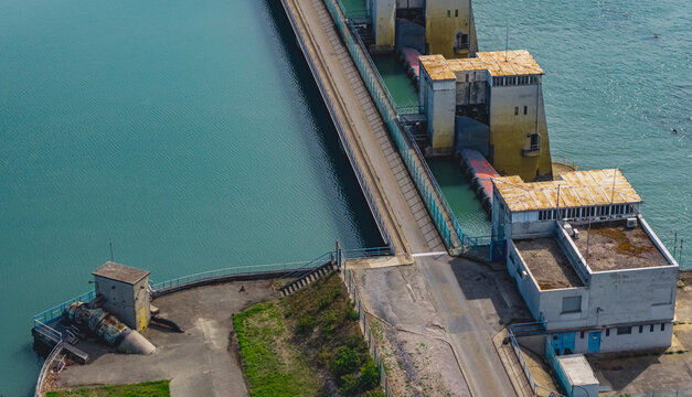 Aerial view of a hydroelectric dam on the Rhone River, featuring industrial infrastructure, spillway structures, and a service road in Le Pouzin, Auvergne-Rhone-Alpes, France.
