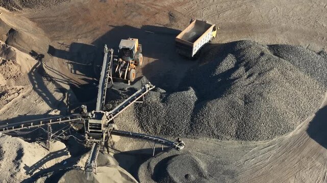 Yellow bulldozer loading construction gravel into a dump truck at an active mining site