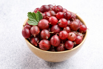 Fresh red gooseberries and green leaf in bowl on grey textured table, closeup © New Africa