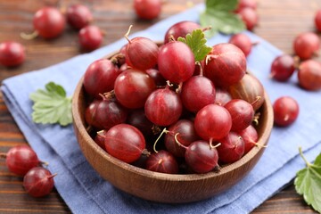 Fresh red gooseberries, green leaves and bowl on wooden table, closeup © New Africa