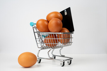 Eggs in a miniature shopping cart with a credit card, symbolizing rising food costs and inflation impacting grocery budgets © Alberto