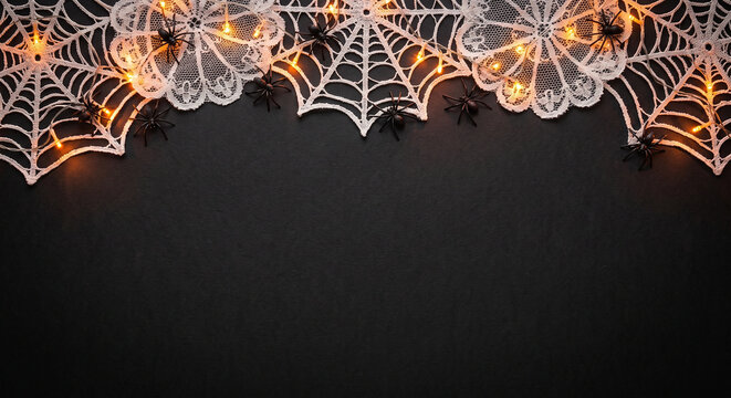 Halloween web decorations with spiders and warm glowing fairy lights on dark backdrop now.