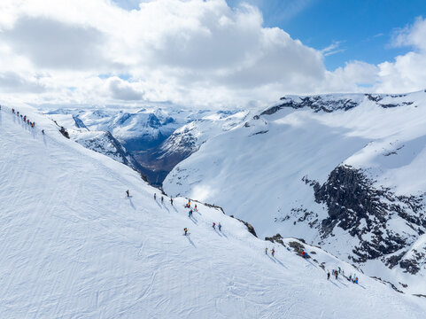 Aerial view of Ringshornet mountain ridge with a group of skiers traversing the snow-covered slopes under a bright sky in Fjord, More og Romsdal, Norway.