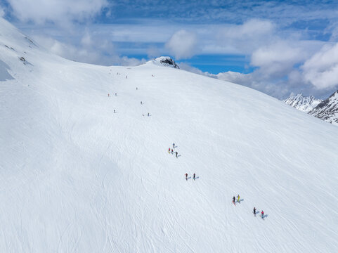 Aerial view of Ringshornet mountain slope with skiers ascending the snowy terrain under a bright blue sky in Fjord, More og Romsdal, Norway.