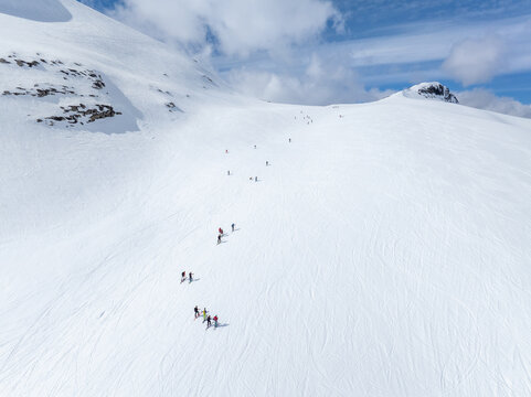 Aerial view of Ringshornet with skiers ascending the snow-covered mountain slope under a bright blue sky in Fjord, More og Romsdal, Norway.