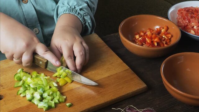 Hands chop green peppers with a knife on a cutting board on the table