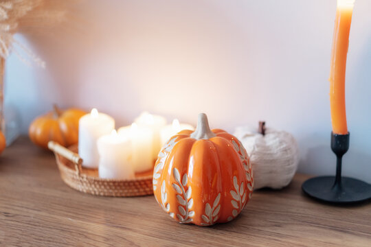 Cozy warm autumn home interior - decorative orange ceramic pumpkins, candles, dried flowers on the wooden console with white wall background. Scandinavian minimalist hygge home fall decor