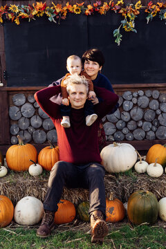 Happy family joyfully sitting on hay with pumpkins on pumpkin patch. Selecting best pumpkins for Thanksgiving and Halloween holidays decoration on farm. Pumpkin harvest. Autumn fall festive mood
