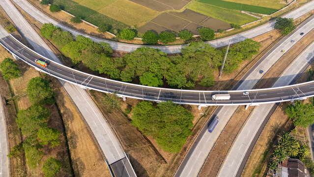 Aerial view of a highway interchange with vehicles driving on the road, surrounded by lush green trees and agricultural fields in Central Java, Indonesia.