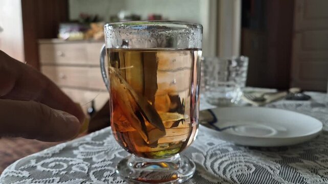 Close-up shot of a hand dipping a tea bag into a glass cup as tea infuses and colors the water