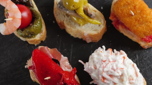 Assorted Spanish pintxos with croquettes, shrimp, olives, tomato, padron pepper and toppings on bread skewers. High quality 4k footage
